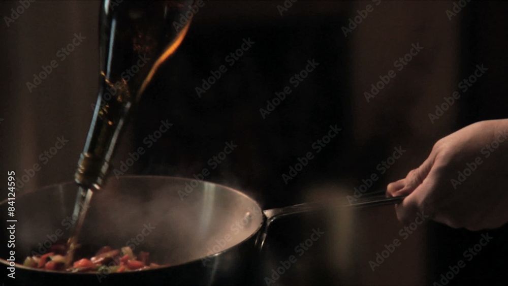 A chef sautéing vegetables and sausage in a pan in a kitchen, with flames A chef sautéing vegetables and sausage in a pan in a kitchen, with flames