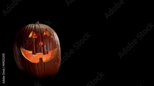 A Jack-o-lantern with a smiling face flickers on a black background