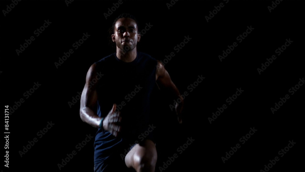 A male athlete runs in place while kicking their legs high in the air in a dark A male athlete runs in place while kicking their legs high in the air in a dark