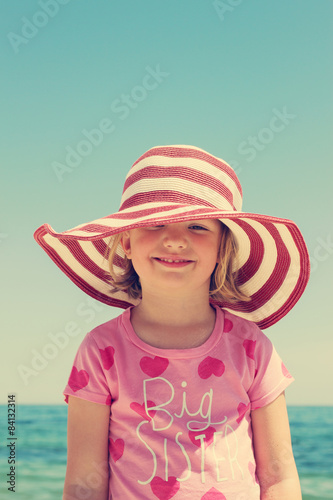 Beautiful little girl in the striped hat on the beach. The image