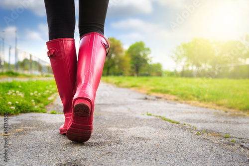 Fotografi Young woman in pink rain boots walking. detail of boots.