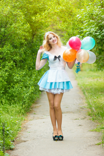 Portrait of a beautiful young blonde woman with long hair dressed as Alice in Wonderland.Girl posing with a big bunch of colorful balloons. Soft focus 