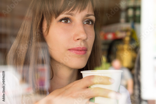Young thinking woman with paper cup of coffee or tea