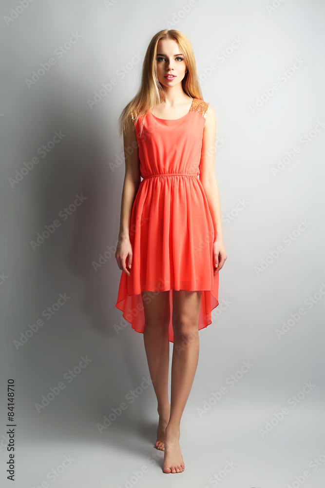 Expressive young model in orange dress on gray background