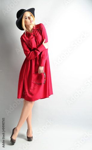 Expressive young model in red dress and black hat on gray background
