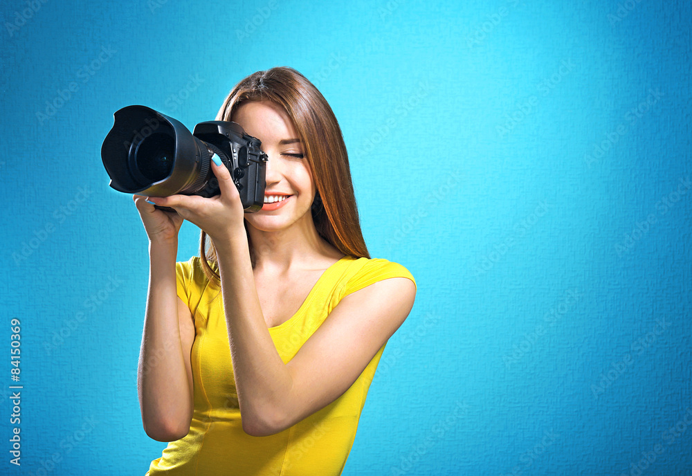 Young female photographer taking photos on blue background Young female photographer taking photos on blue background