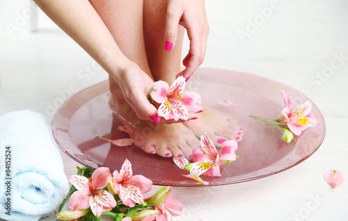 Woman washing beautiful legs in bowl, on light background. Spa procedure concept