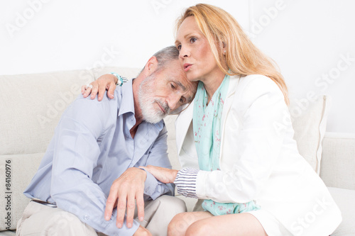 Elderly man giving support to his partner while sitting on sofa