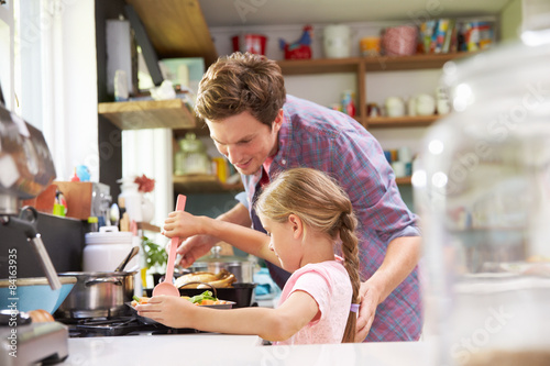 Daughter Helping Father To Cook Meal In Kitchen © Monkey Business