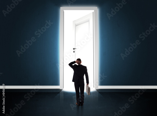 Business man looking at big bright opened door