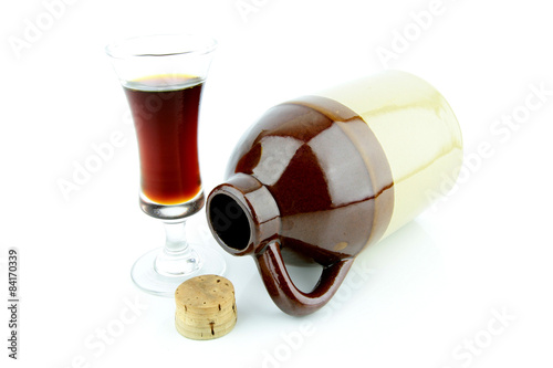 Old clay jug with a cork used to hold booze, with a filled glass next to it.