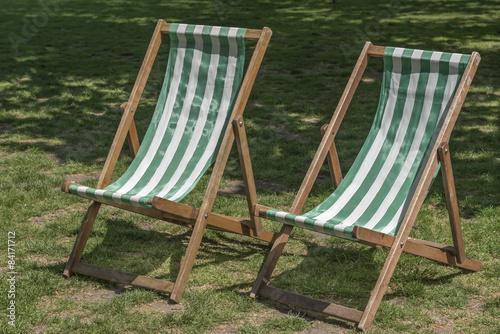 A pair of empty wooden deckchairs in a park in the summer sun
