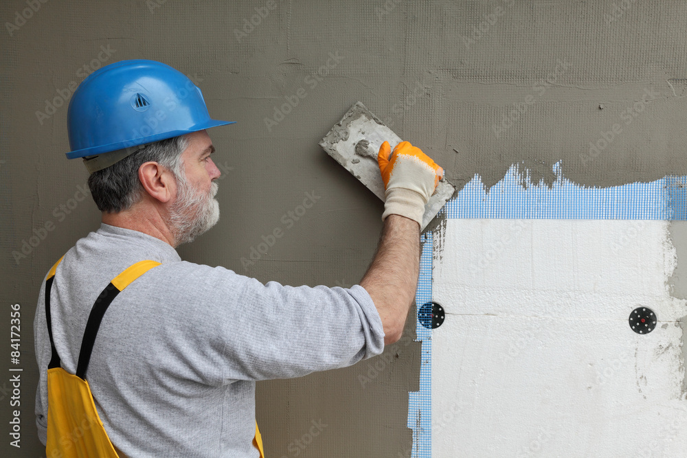Wall insulation worker spreading mortar over mesh and styrofoam Wall insulation worker spreading mortar over mesh and styrofoam