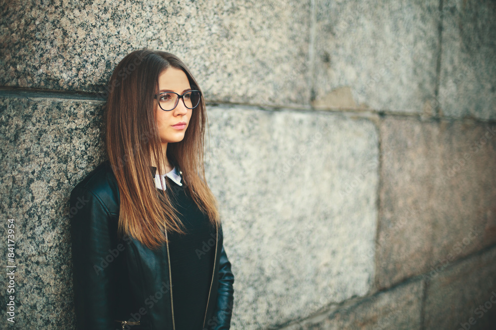 Portrait of a young hipster student girl with glasses thinking near the wall of college