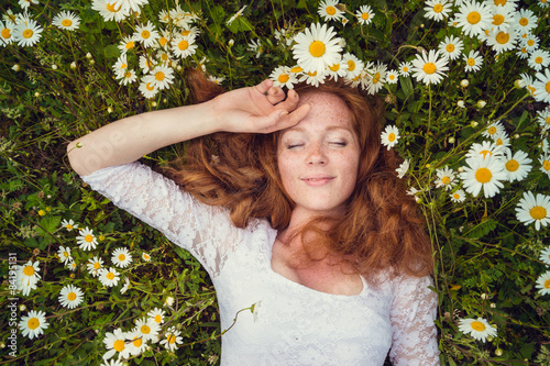 Beautiful young girl with curly red hair in camomile field