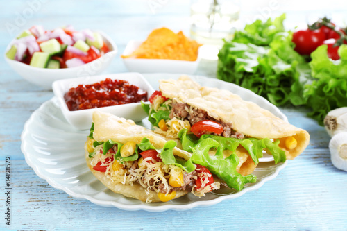 Tasty taco with tomato dip on plate and vegetables on table close up