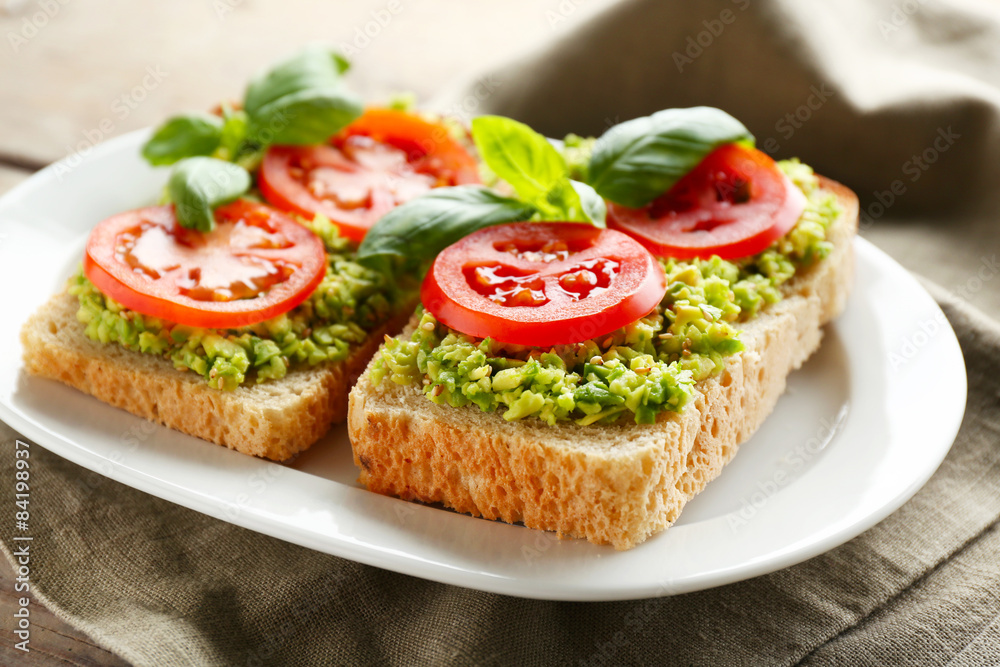 Vegan sandwich with avocado and vegetables on plate, on wooden background Vegan sandwich with avocado and vegetables on plate, on wooden background
