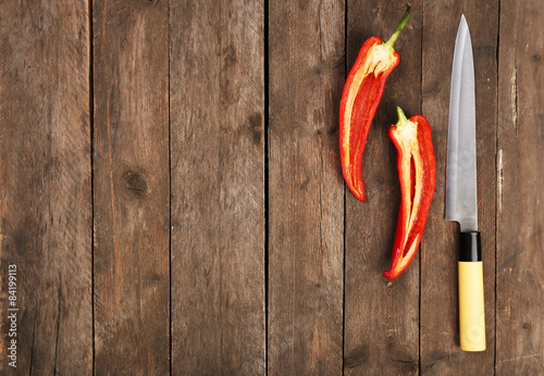 Halves of pepper chili with knife on wooden background