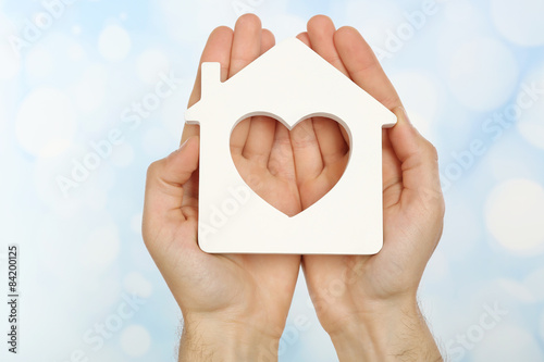 Female hands holding house on light blurred background