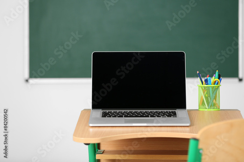Wooden desk with stationery and laptop in class on blackboard background