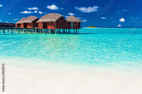 Overwater bungalow and beach in blue lagoon of tropical Maldives