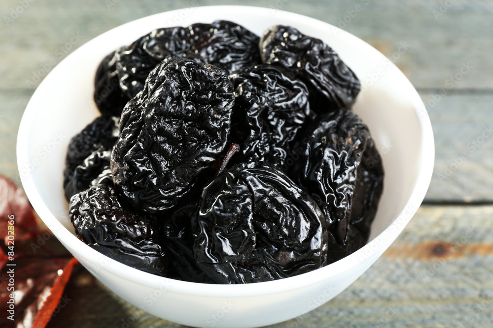 Saucer of prunes with leaves on wooden table, closeup Saucer of prunes with leaves on wooden table, closeup