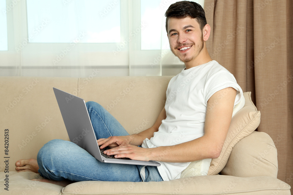 Handsome young man sitting on sofa and using laptop in room Handsome young man sitting on sofa and using laptop in room