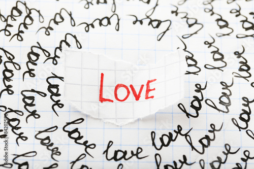 Word LOVE written on torn paper on sheet of paper background