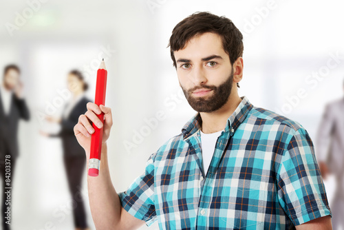 Young man holding big red pencil.