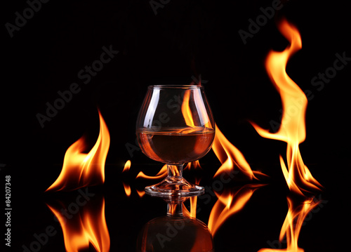Hot chili pepper in a cognac ballon with a fire on a black background