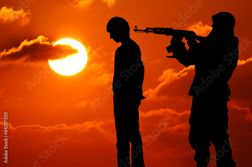 Silhouette of man with rifle pointed at victim's back