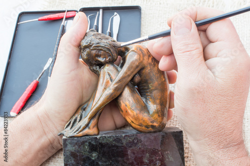 Obraz na plátně Hands of sculptor hold copper sculpture and clean it with brush