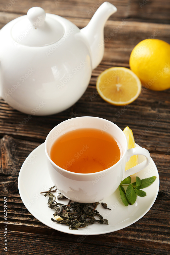 Cup with green tea and teapot on brown wooden background