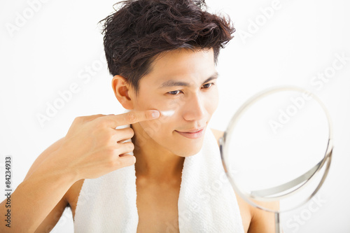 Konstfotografi smiling man applying cream lotion on face