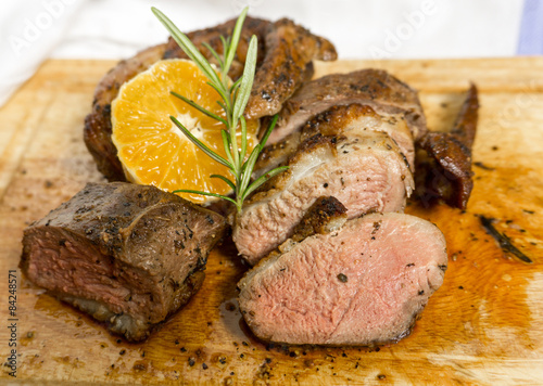 Slices of duck breast with rosemary and slice of orange on board