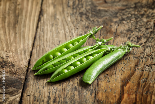 Opened green pea pods with peas in an old wooden table, selectiv photo