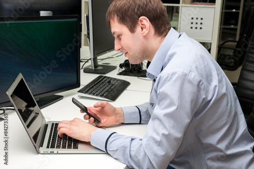 Young handsome happy man with computer in the office. Programmin photo