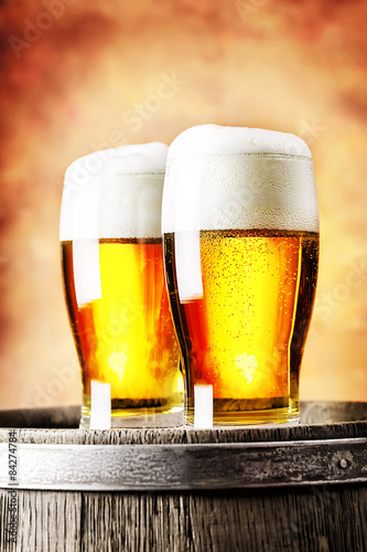Two glasses of light beer standing on a wooden barrel
