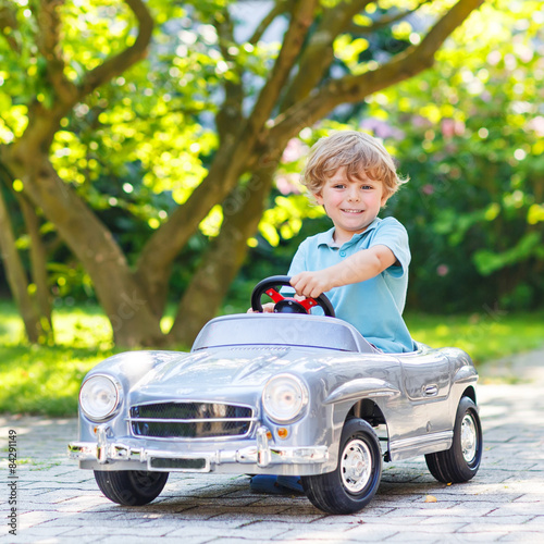 Little boy driving big toy old car, outdoors