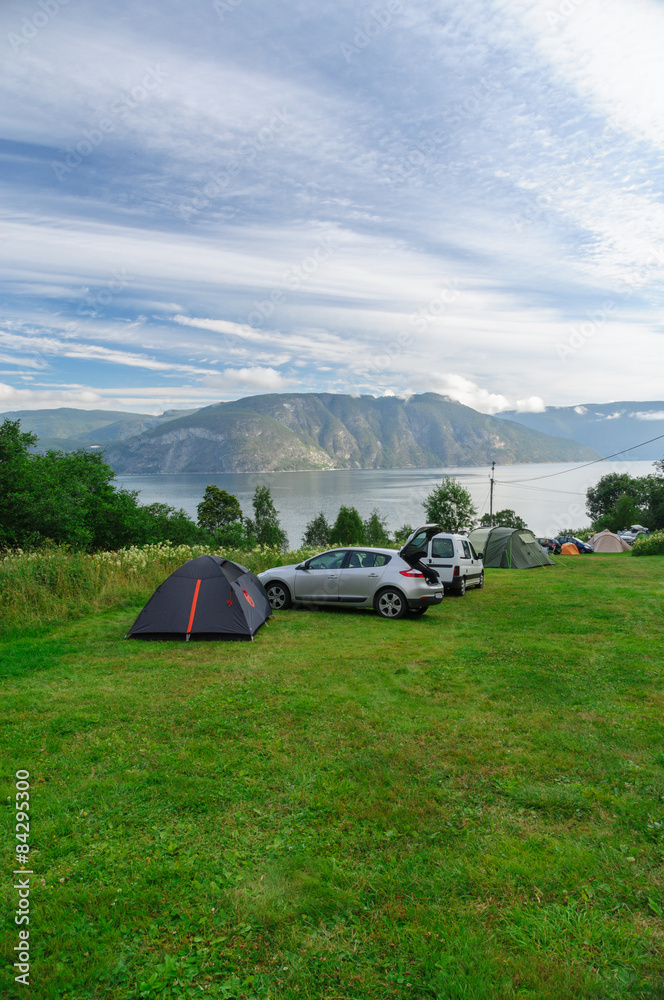 Camping area near fjord with cars and tents on grass