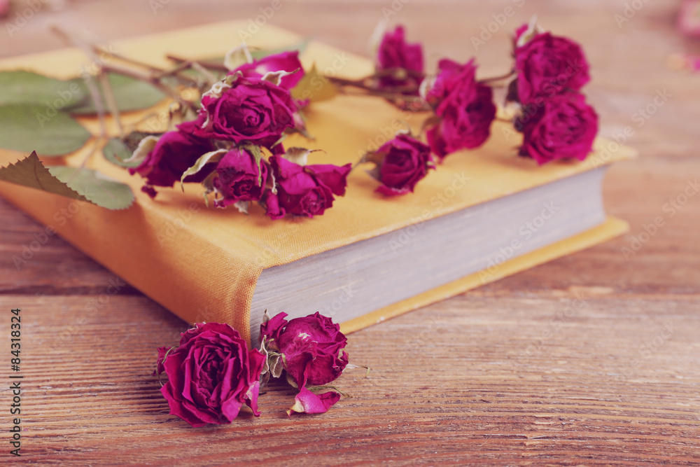Dried roses with book on wooden table, closeup Dried roses with book on wooden table, closeup
