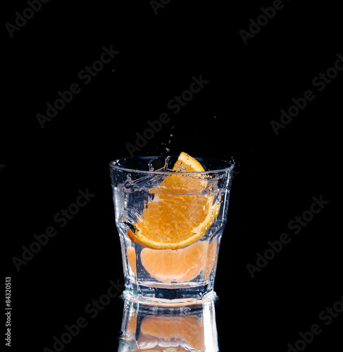 Slice of lemon splashing into a glass of water with a spray of water droplets 