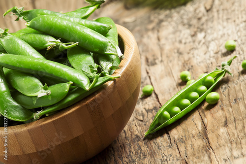 Pods of fresh green peas in a bowl on old wooden table, selectiv photo