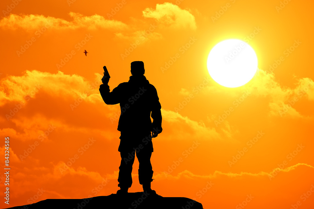 Silhouette shot of soldier holding gun with colorful sky and mountain in background
