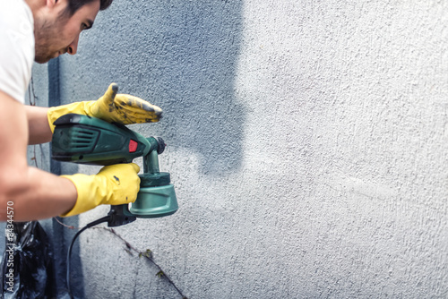 Man painting a grey wall, renovating exterior walls of house photo