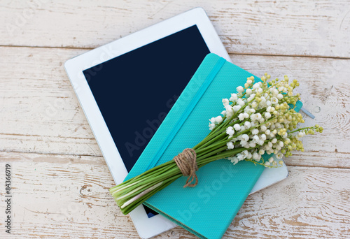 diary, a tablet computerand  lilies of valley on the table photo