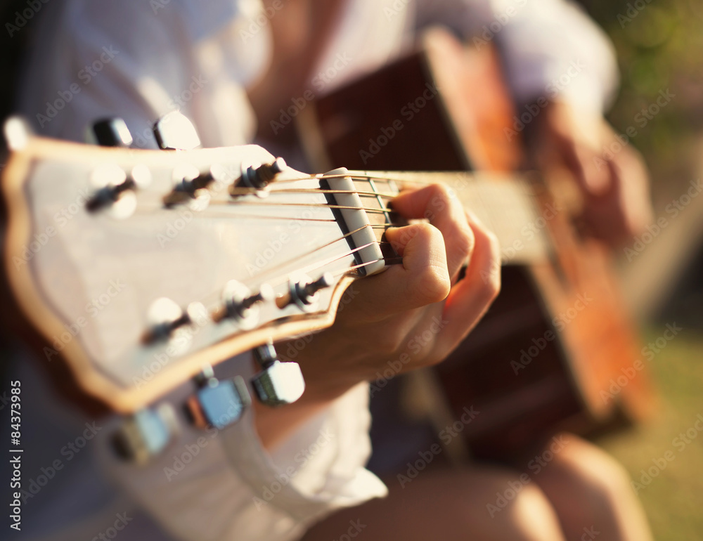 Obraz premium Young woman in sun park holding a guitar and playing music