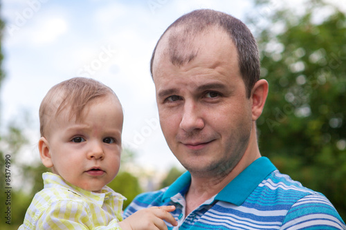 father holds a small child in his arms, outdoors in a park
