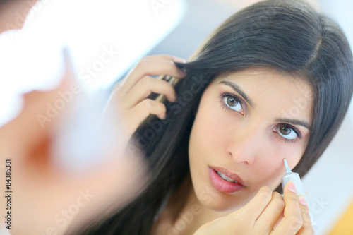 Beautiful brunette woman applying concealer