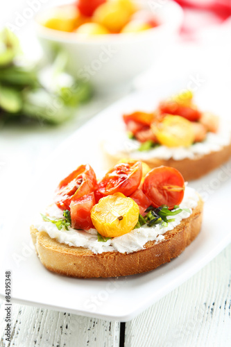 Tasty fresh bruschetta with tomatoes on plate on white wooden ba